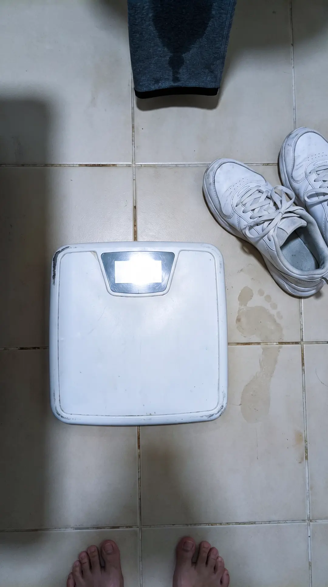 Une balance au sol, à côté d'une paire de baskets encore lacées, dans une entrée sobre.